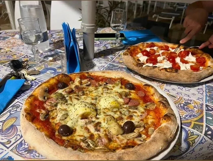 Due pizze del Golden Beach appena sfornate, su tovaglia con motivo maiolica